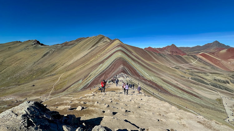 The striped red, ochre and green slopes of Rainbow Mountain under a blue sky
